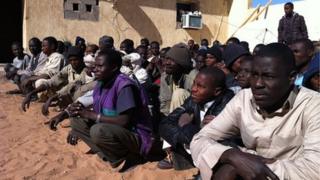 A large group of migrants sitting in rows on the ground