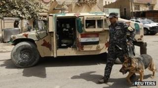 A police officer walks a sniffer dog at a checkpoint in Baghdad (26 March 2012)