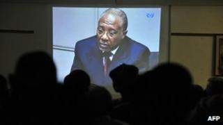 People watch the trial of Liberian ex-leader Charles Taylor (on screen) taking place in the Hague, inside the Special Court in Freetown, Sierra Leone on Friday