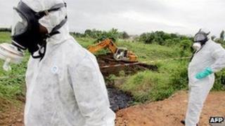 Two civil protection workers pass by a bulldozer clearing a site polluted with toxic waste at the Akouedo district in Abidjan - 19 September 2006
