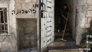 A man clears debris from the entrance to a flat in Jerusalem following a suspected arson attack. The grafitti says: "Get out of the neighbourhood" (4 June 2012)