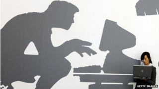 Женщина с ноутбуком стоит перед стеной с компьютерной росписью