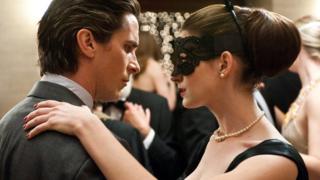 A publicity photograph from The Dark Knight Rises. Christian Bale as Bruce Wayne dances at a ball with Anne Hathaway (Catwoman). She is wearing a mask over her eyes.