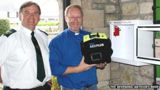 Gerard Rothwell o Wasanaeth Ambiwlans Cymru a'r Parchedig Anthony Beer gyda'r diffribilydd