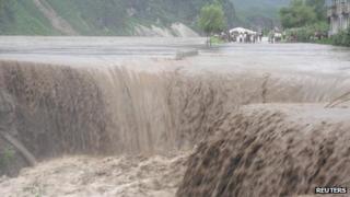 A handout photo from the Red Cross dated 24 July, 2012 shows North Korean residents standing next to a road as flood water pours into a caved-in area in Songchon county, South Pyongan Province