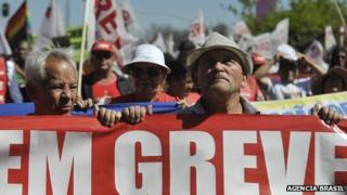 Striking public sector workers in Brazil hold up sign saying "On strike"