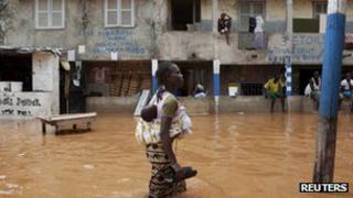 A woman with a baby on her back wades through water after overnight flooding on a street in Senegal's capital Dakar, August 14, 2012