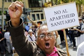 An immigrant holds a banner reading "No to the healthcare apartheid" in Madrid, 1 September