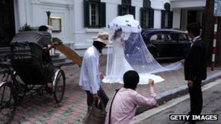A photographer positions a bride for a picture for her wedding photo album in front of a colonial style hotel, rickshaw and old cars in downtown Hanoi on August 26, 2010.