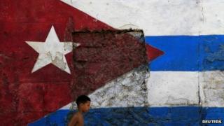 Child walks past a Cuban flag painted on wall in Havana