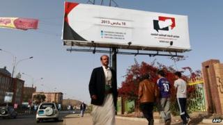 Men walk past a poster advertising the national dialogue conference in Sanaa (14 March 2013)