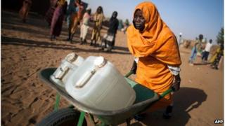 Sudanese woman pushing jerry cans of water in a camp for displaced people, Darfur, March 2013