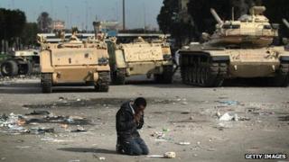 An anti-government demonstrator prays near Egyptian army vehicles on 3 February 2011 amid protests that eventually swept away the regime of Hosni Mubarak