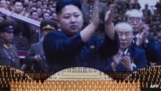 North Korean performers sit beneath a screen showing images of leader Kim Jong-Un at a theatre during celebrations to mark the 100th birth anniversary of the country's founding leader Kim Il-Sung, in Pyongyang on 16 April 2012.