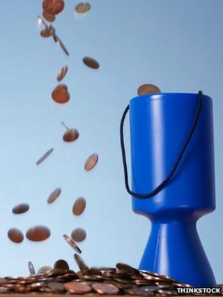 coins dropping next to a charity's collecting tin