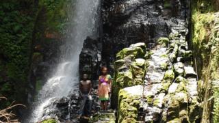 A boy and girl stand in front of the sacred waterfall