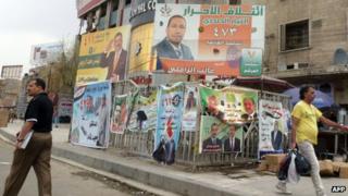 Iraqi men walk past provincial elections campaign poster in Baghdad
