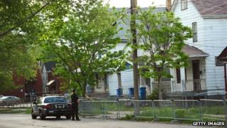 A Cleveland police officer stands watch in front of the house on Seymour Street where three women were held captive for a decade