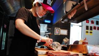 Chu Mingying cutting a pie in Gung Ho pizza shop