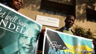Well-wishers from South Africa and the Bahamas stand with signs outside the Mediclinic Heart Hospital where former South African President Nelson Mandela, 94, has spent the previous the week June 16, 2013 in Pretoria, South Africa.