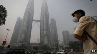 Пешеход в маске ждет пересечения главной дороги перед башней-близнецом Петронас, покрытой дымкой в ??Куала-Лумпуре, Малайзия, 24 июня 24 года 2013 г.