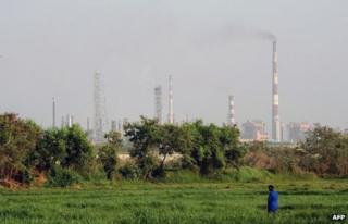 На этой фотографии, сделанной 22 апреля 2013 года, индийский мужчина стоит в поле, как заводские трубы из тени промышленной зоны на заднем плане в Мумбаи.