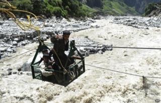 A local man throws a rope as he and others riding a gondola cross the Alaknanda river from the Hemkund Sikh temple to Govindghat following flash floods in Uttarkhand state on June 30, 2013