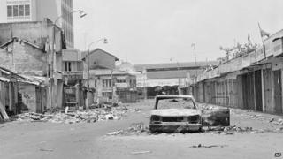 An abandoned burnt out automobile and street filled with rubble, Colombo, July 30 1983