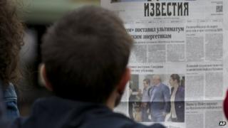 street cafe visitor reads a fresh Russian newspaper "Izvestia" with a front page pictures of Russian lawyer Anatoly Kucherena, centre, and National Security Agency leaker Edward Snowden, centre left