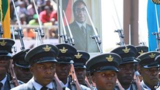 Soldiers march with a photo of Zimbabwean President elect, Robert Mugabe, in the background, during the country"s commemoration of Defence Forces Day,