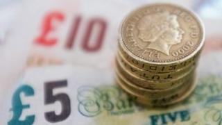 A stack of pound coins on top of £5 and £10 notes