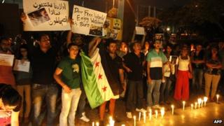 Lebanese and Syrian civilians hold signs and Syria's former independence flag as they take part in a candle-lit vigil in front of the offices of the United Nations headquarters in Beirut
