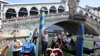 Gondoliers pay their respects, as people line the bridge, in front of the place near Rialto bridge where a German tourist was killed in Venice taken on 18 August 2013
