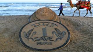 An Indian walks past a sand sculpture of a rupee coin on a beach in Puri, India, on 22 August