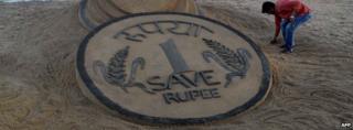 A rupee coin sketched in sand
