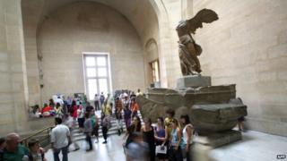A picture taken on 17 June, 2009, shows people posing in front of the Winged Victory of Samothrace sculpture as they visit the Louvre museum in Paris.