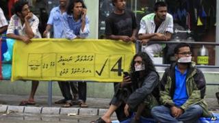 Supporter of Maldives former president Mohammed Nasheed with their mouths covered with tape sit near a campaign poster of Nasheed during a silent protest in Male, Maldives, Monday, Oct. 21, 2013