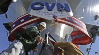 Shipbuilding workers Stephen Gilliland, left, and John Gies, right, prepare the for the christening of the Navy's newest nuclear powered aircraft carrier USS Gerald R Ford at the shipyard in Newport News, Va., Friday, Nov. 8, 2013