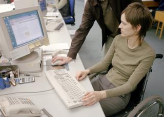 Woman in wheelchair and standing man look at computer screen. Posed photograph