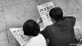 Two people in a Washington, DC, park read news of John F Kennedy's assassination.