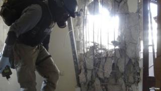 A UN chemical weapons expert, wearing a gas mask, inspects one of the sites of an alleged chemical weapons attack in the Damascus" suburb of Zamalka