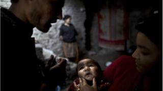 Pakistani Sonya Javed, 20, right, holds her son Shahzeb, 1, to receive a polio vaccine by a health worker at her home in Islamabad, Pakistan, Tuesday, Nov. 26, 2013