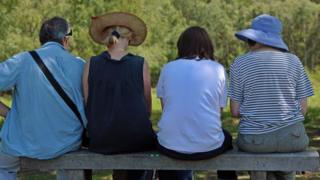 A grandmother, her grandson and two parents sitting on a bench in the countryside