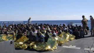 Migrants sit in an Italian navy vessel off the coast of Sicily (2 January 2014)