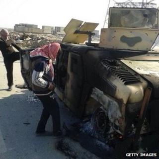 Iraqis inspect the burnt out remains of an Iraqi army APC on the highway leading to Ramadi