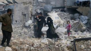 People walk on rubble of collapsed buildings at a site hit by what activists said was barrel bombs dropped by government forces in Aleppo's Dahret Awwad neighbourhood on 29 January 2014