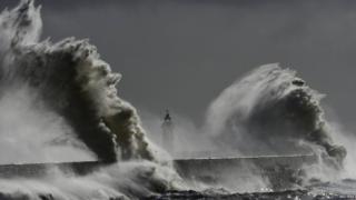 Большие волны обрушиваются на маяк и гавань во время прилива в Ньюхейвене в Сассексе