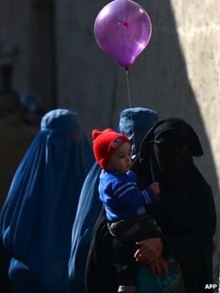 An Afghan burka-clad woman walks with her child holding a balloon in Kabul on 15 February 2014
