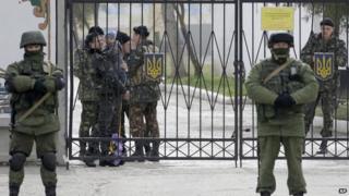 A Ukrainian soldier with a child 2nd left, watches Russian soldier guard the gate of an infantry base in Perevalne, Ukraine,
