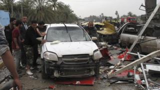 People push a damaged car at the scene of a suicide attack in the city of Hilla, 9 March